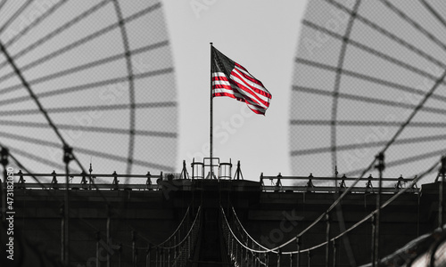 The national flag of United States of America winding on top of Brooklyn Bridge landmark from Manhattan. One of the most visited places in America. Symbol of patriotism. © Dragoș Asaftei