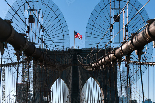 The national flag of United States of America winding on top of Brooklyn Bridge landmark from Manhattan. One of the most visited places in America. Symbol of patriotism.