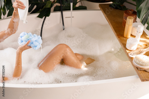 Fotografie Female hands pouring shower gel from bottle onto loofah sponge