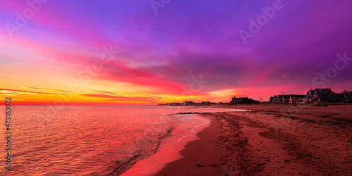 Vibrant saturated pink and blue seascape at sunrise. Curved beach  gentle waves  dramatic clouds over the coastal village. Stunning red twilight landscape over Falmouth Height Beach on Cape Cod.