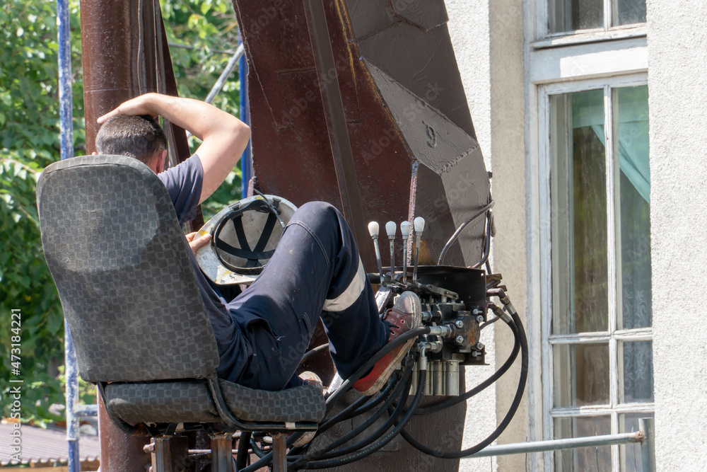 Obraz premium The operator driver sits in the open cabin of the tower crane behind the control levers of the hydraulic drive of various systems. Control panel levers for lifting operation of mobile crane truck