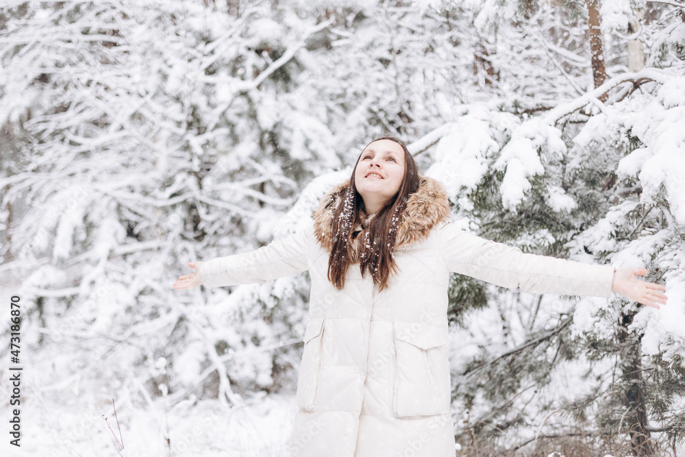 Winter portrait of young woman. Happy girl walking in winter forest and looking snow falling down. Christmas and New year holidays. Slow life. Cute lady in warm clothing having fun in nature outdoors. Winter portrait of young woman. Happy girl walking in winter forest and looking snow falling down. Christmas and New year holidays. Slow life. Cute lady in warm clothing having fun in nature outdoors.