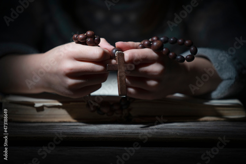 Close up portrait of little child girl praying with wooden rosary. Horizontal image.