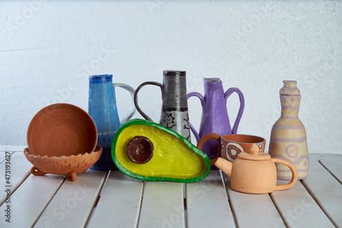 Crafts made of clay. A kettle, jugs, plates, an avocado-shaped dish on a wooden table. Light background photo