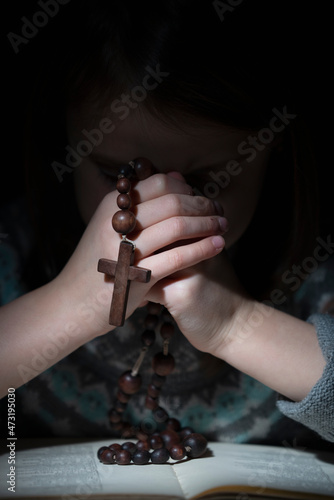 Portrait of little child girl praying with wooden rosary. Vertical image.