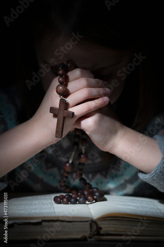 Portrait of little child girl praying with wooden rosary.