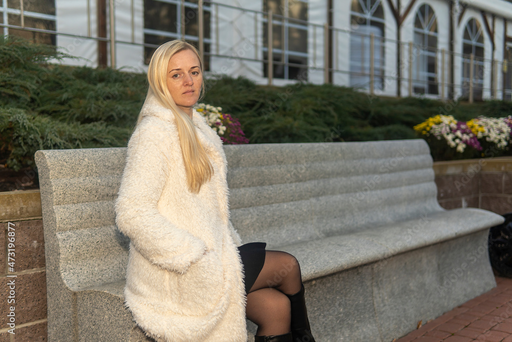 portrait of a blonde girl on a bench in a white fur coat in a city park in autumn portrait of a blonde girl on a bench in a white fur coat in a city park in autumn