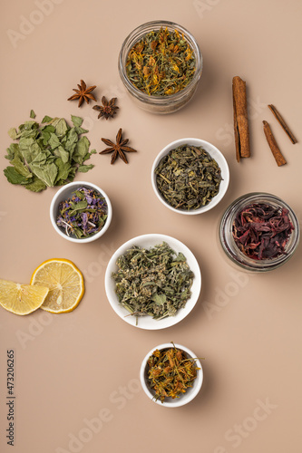 Different types of tea and herbs in bowls on a beige background