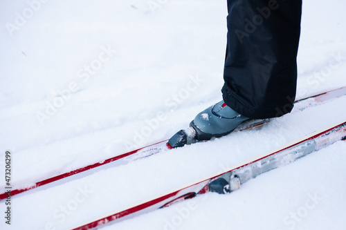Man is skiing. Close-up of legs in gray ski boots on skis, man riding in snow on clear sunny day, side view. 