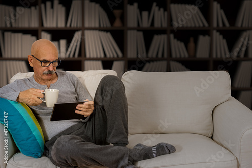 Senior Male Reading in a Digital Tablet Sitting at the Sofa at the House Living Room
