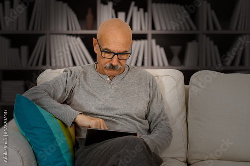 Senior Male Reading in a Digital Tablet Sitting at the Sofa at the House Living Room