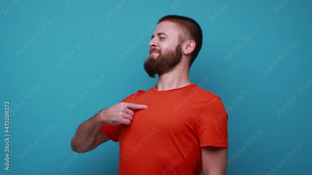 Bearded man pointing himself and looking with arrogant selfish expression, feeling successful and self-important, wearing orange T-shirt. Indoor studio shot isolated on blue background. Bearded man pointing himself and looking with arrogant selfish expression, feeling successful and self-important, wearing orange T-shirt. Indoor studio shot isolated on blue background.