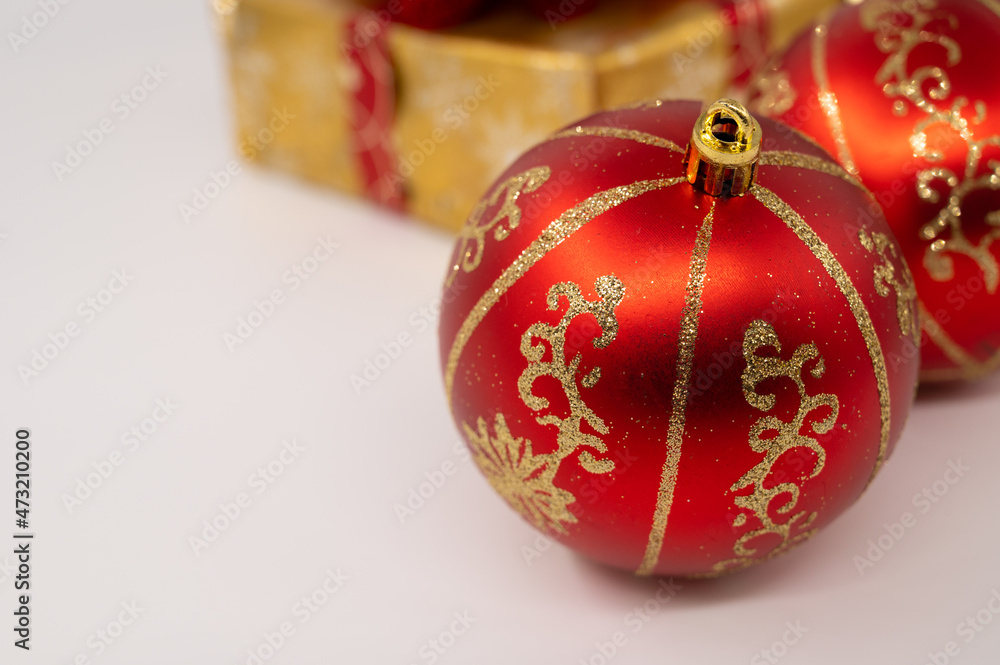 Close-up of a red Christmas bulb with golden stripes on it. Golden gift box in background. Isolated white background.