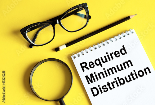 Required minimum distributions RMD phrase written on a notebook with glasses, magnifying glass and pencil photo