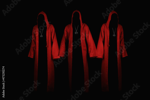 Group of mystery people in a red hooded cloaks.  Unrecognizable person. Hiding face in shadow. Ghostly figure. Satanic sect member. Conspiracy concept. Isolated on black.