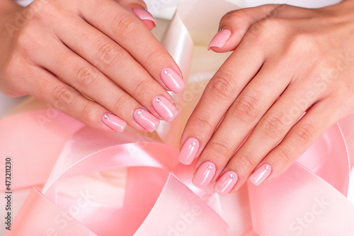 Female hands with wedding manicure nails  nude gel polish  on pink ribbons background