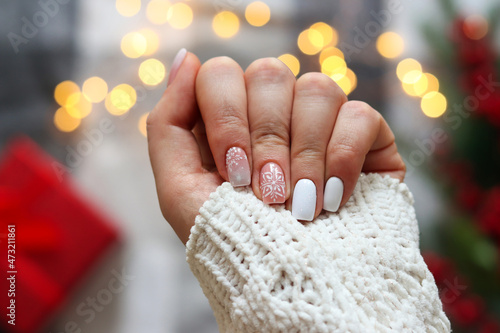 Idea of the winter manicure. Woman\'s hand with gel polish manicure white color and with snowflakes ornament against festive Christmas background. Selective focus