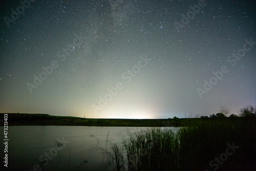 milky way and lake and reeds stars over the lake at night lights . Lake over the nightsky
