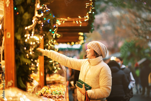 Fotografia Outdoor portrait of young woman buying sweets at Christmas market