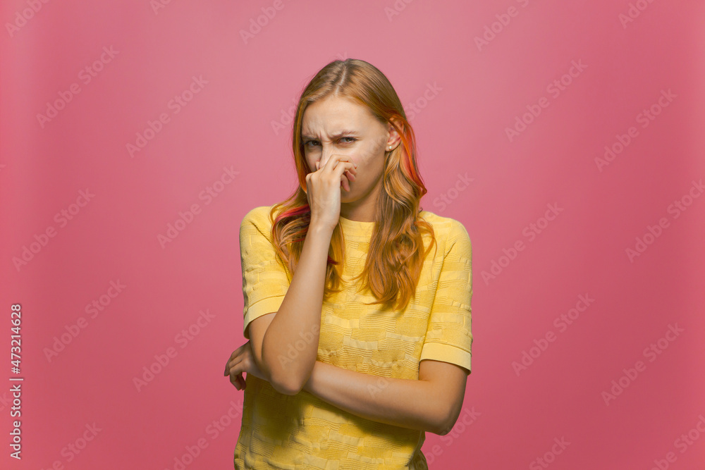 Bad smell. Young girl holding breath with fingers on nose from stinky odor on pink studio background. Parosmia problem Bad smell. Young girl holding breath with fingers on nose from stinky odor on pink studio background. Parosmia problem