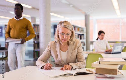 Woman with books sits at table in the library. High quality photo