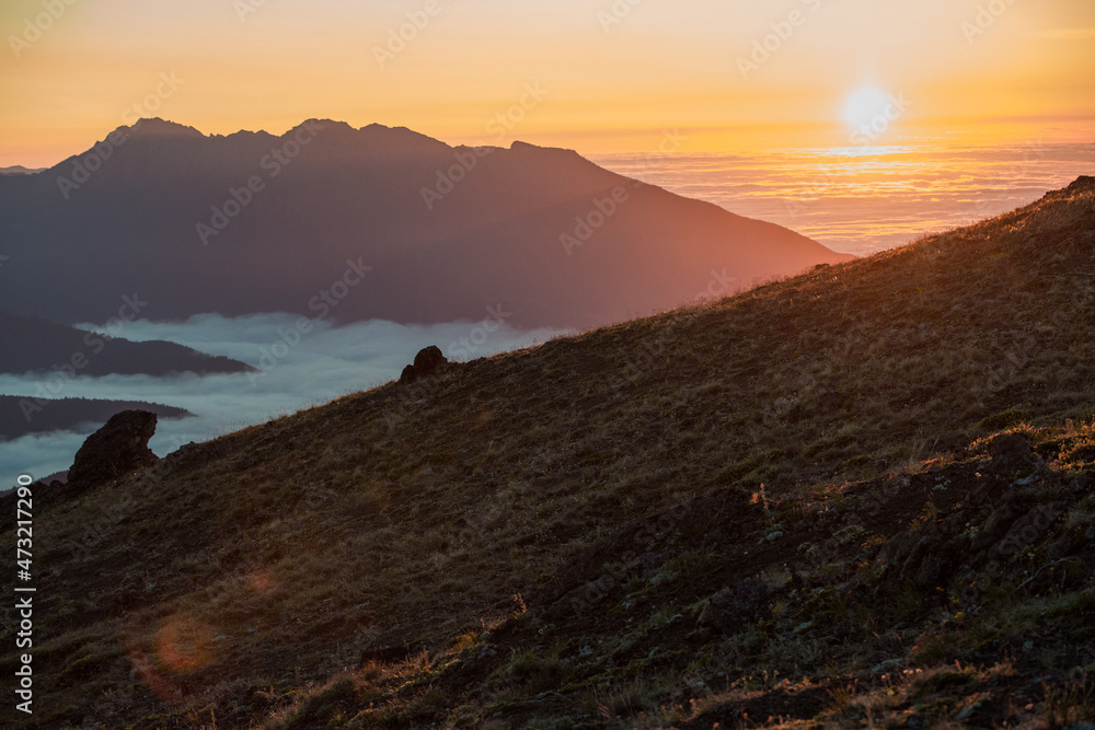 Obraz premium orange sunset on a mountain over a sea of clouds in the valley below