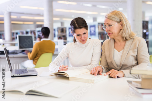 Female teacher working with girl student in university library. High quality photo