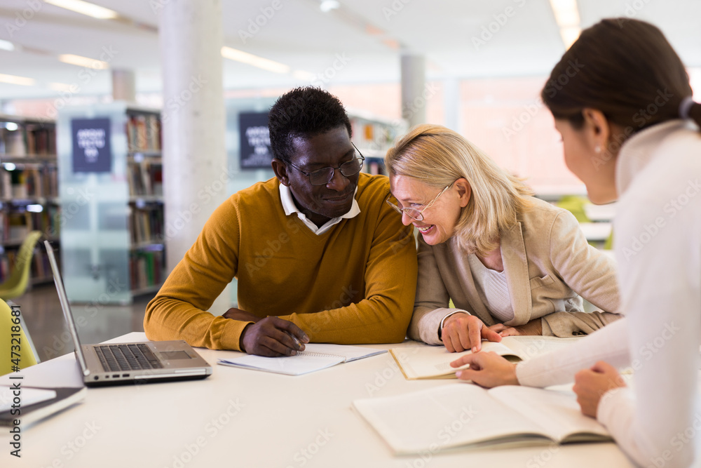 Obraz premium Students sitting in library, working with professor. High quality photo
