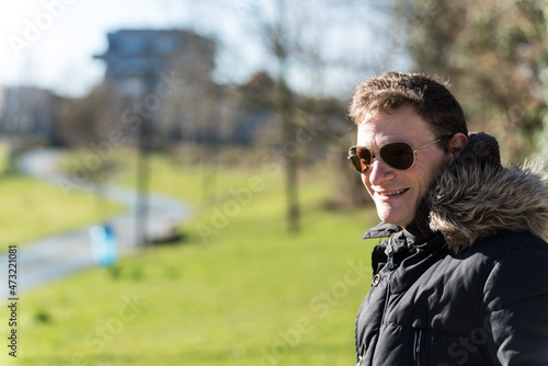 Outdoor portrait of a manman with a furry winter coat coat, wearing sunglasses standing in a Brussels park