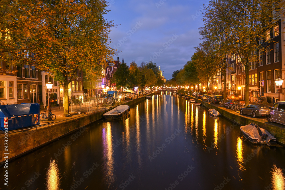 Buildings, trees and canal in Amsterdam at night. City of Amsterdam, Holland. Dutch houses. 
