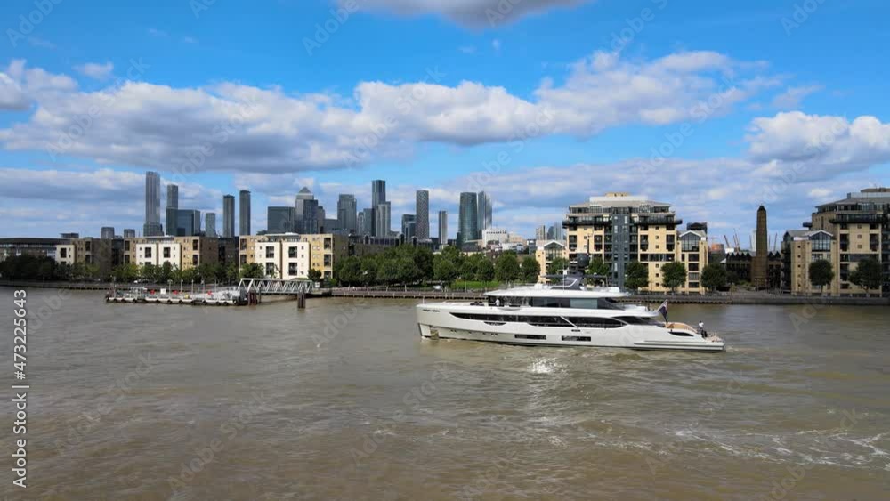 Side tracking of luxury yacht cruising at Thames river. Modern skyscrapers in business hub in background. London, UK Side tracking of luxury yacht cruising at Thames river. Modern skyscrapers in business hub in background. London, UK