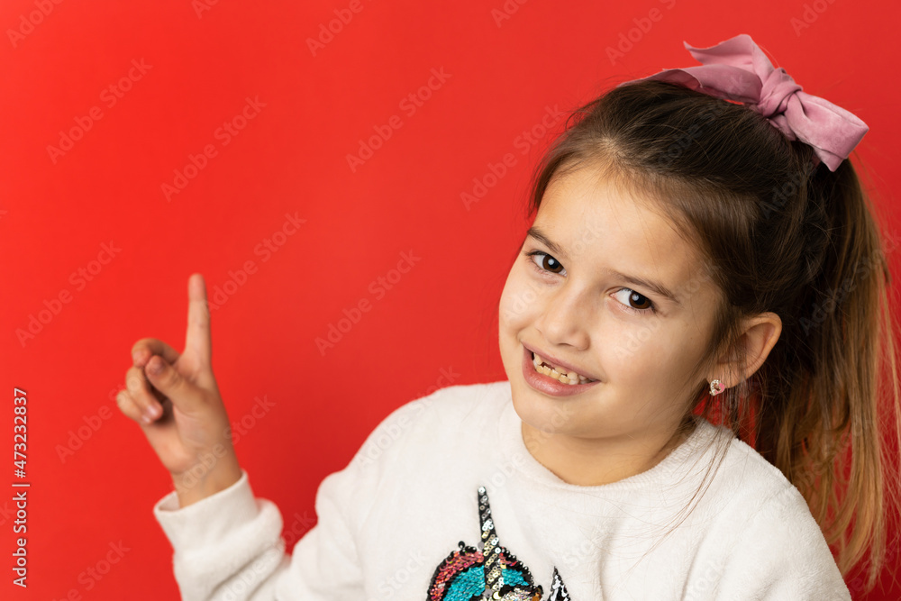 Front view studio shot of one caucasian girl in front of red background holding finger showing to copy space Front view studio shot of one caucasian girl in front of red background holding finger showing to copy space