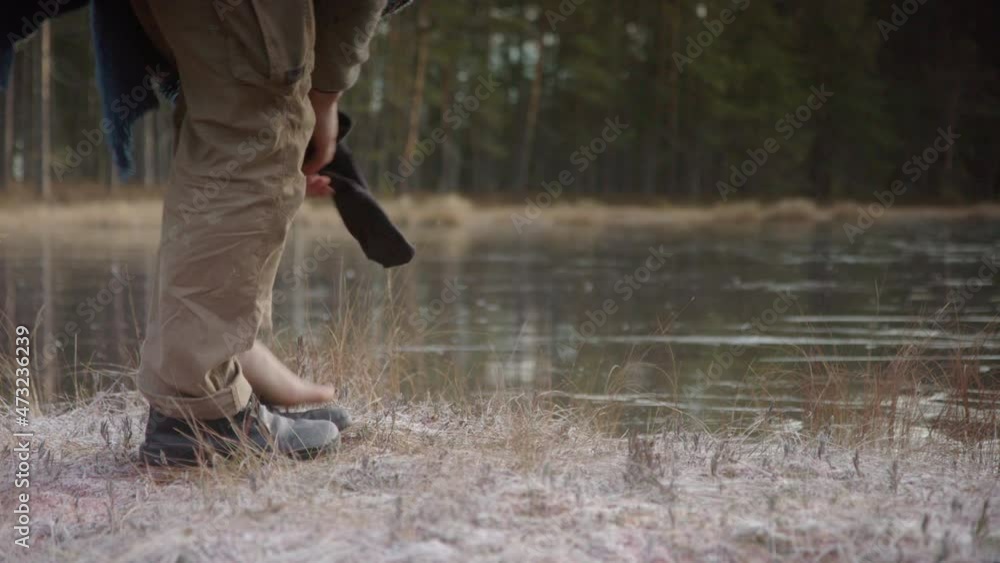 TRACKING shot of an ice bather removing shoes and socks in front of frozen lake TRACKING shot of an ice bather removing shoes and socks in front of frozen lake