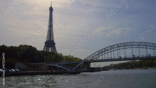 Tracking shot over the Seine river with people crossing the Passerelle Debilly with the Eiffel Tower behind in Paris. photo