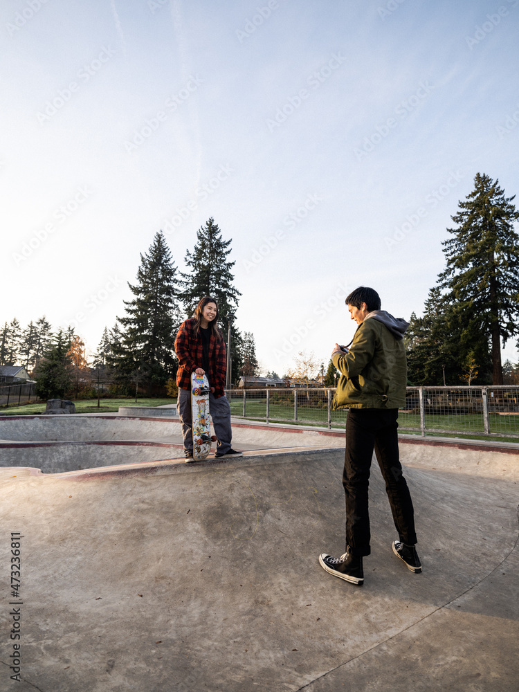 Young Indigenous male photographer and nonbinary skater outdoors Stock