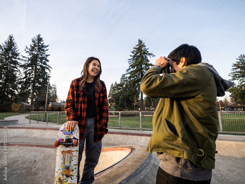 Young Indigenous male photographer and nonbinary skater outdoors Stock
