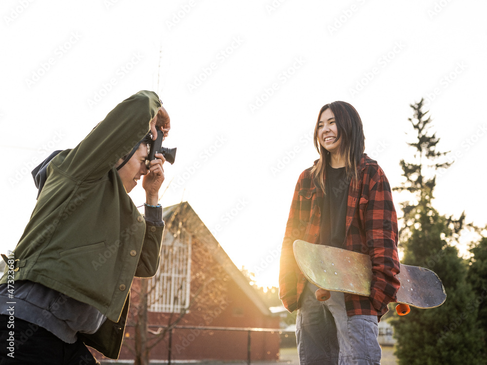 Young Indigenous male photographer and nonbinary skater outdoors Stock