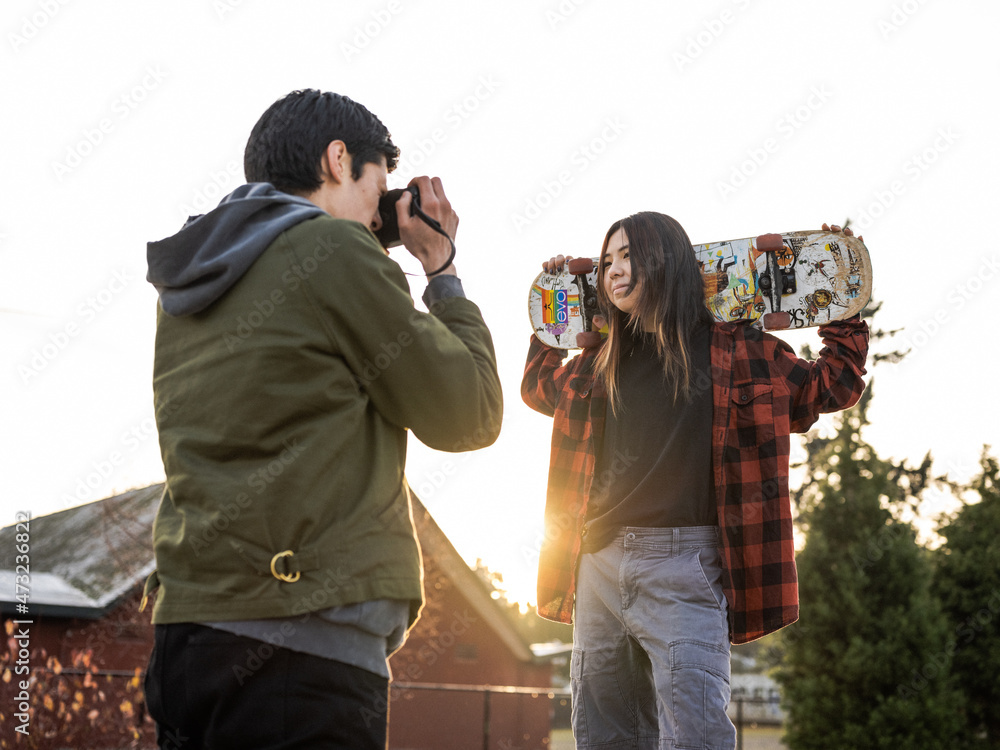 Young Indigenous male photographer and nonbinary skater outdoors Stock