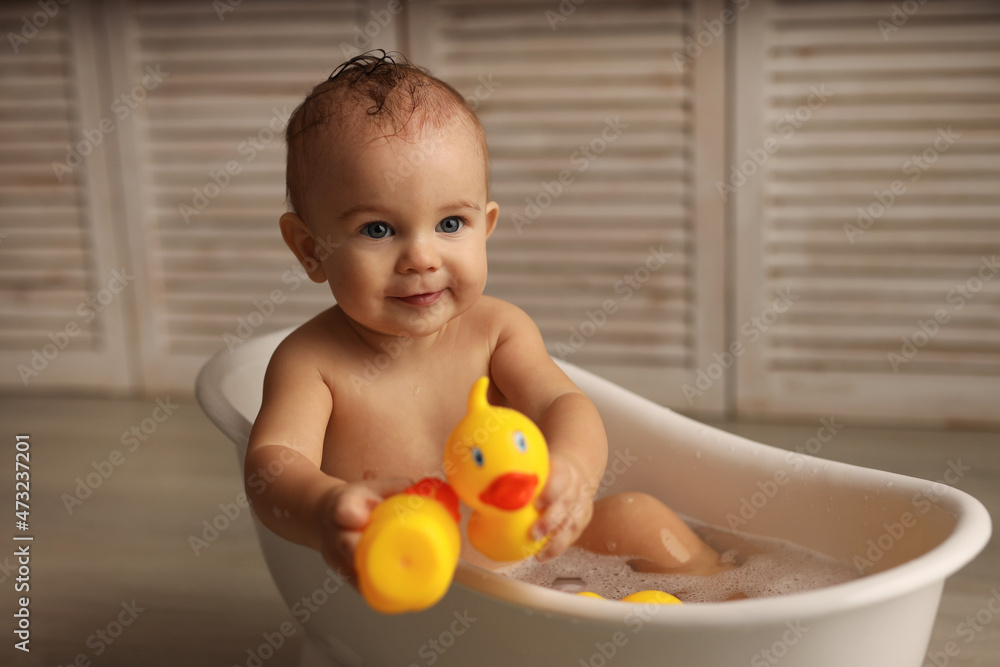 a baby of 11 months is bathing in a white baby bath with rubber ducklings, the baby is laughing, the concept of children's goods. high-quality photography a baby of 11 months is bathing in a white baby bath with rubber ducklings, the baby is laughing, the concept of children's goods. high-quality photography