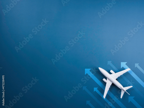 Heading arrows moving beside the white plane model on blue background with copy space, top view, minimal style. White airplane, flat lay design. Flight, travel concept.