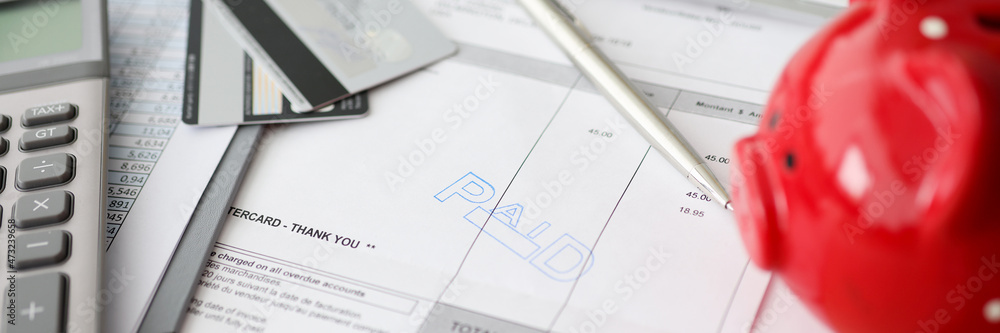 Paid words and calculator with a piggy bank on counting paper for payment closeup