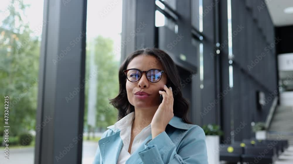 Closeup of young businesswoman talking on phone and showing joy, walking in office building spbi. Portrait of American African female has mobile talk and looks with smile, holds smartphone in hand and Closeup of young businesswoman talking on phone and showing joy, walking in office building spbi. Portrait of American African female has mobile talk and looks with smile, holds smartphone in hand and