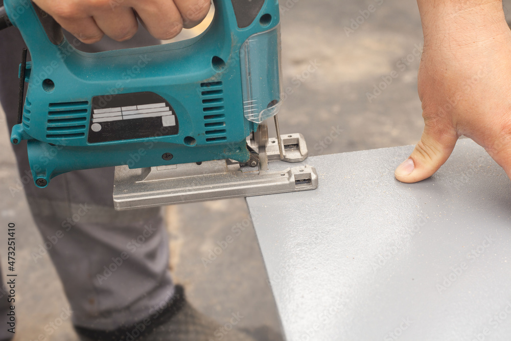 Men's hands with an electric jigsaw saw a gray board