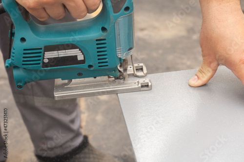 Men's hands with an electric jigsaw saw a gray board