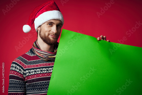 handsome man in a santa hat holding a banner holiday red background © SHOTPRIME STUDIO