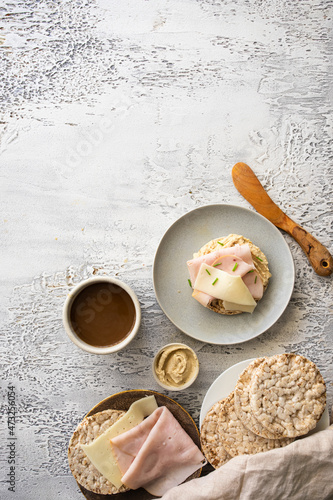 Modern healthy breakfast. Crispy buckwheat and rice cake with hummus, ham and cheese and hot drink on white table at the morning.