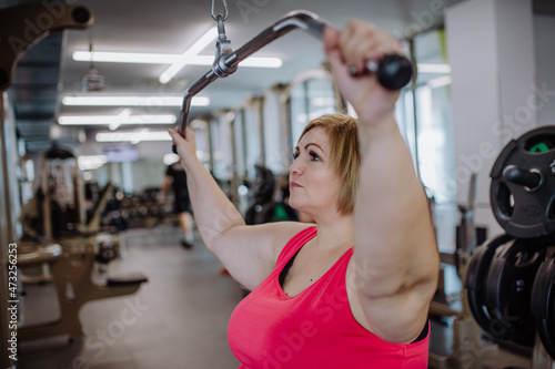 Mid adult plus size woman working out on a lat pulldown machine indoors in gym photo