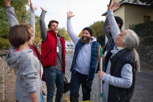 Diverse group of happy community service volunteers raising hands together outdoors in street