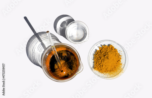Organic Curcuma Powder in Chemical Watch Glass, Ferric Chloride Liquid with stirring rod and Crystal clear liquid in Beaker. Closeup chemical ingredient on white laboratory table. Top View photo