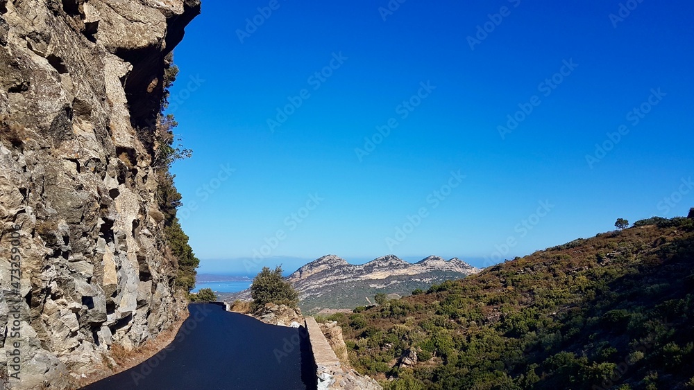 Narrow winding mountain road in Balagne with breathtaking views of Patrimonio hills on a clear, sunny morning. Corsica, France.